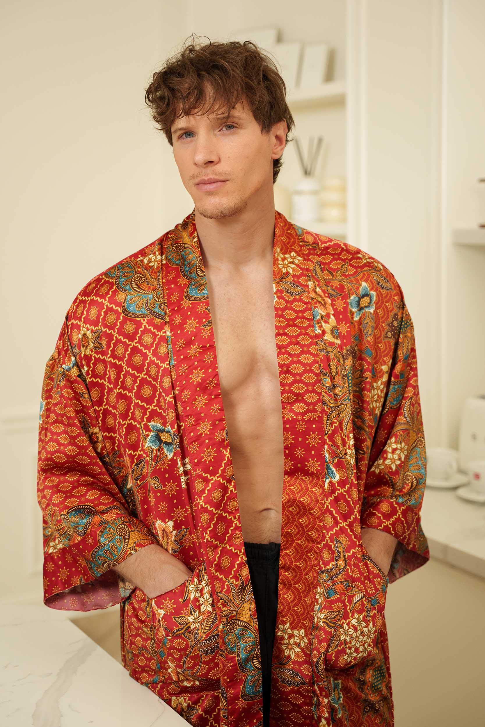 Close-up of Toré Senja men’s kimono robe – detailed floral batik pattern on warm red satin fabric.