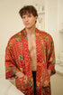 Close-up of Toré Senja men’s kimono robe – detailed floral batik pattern on warm red satin fabric.