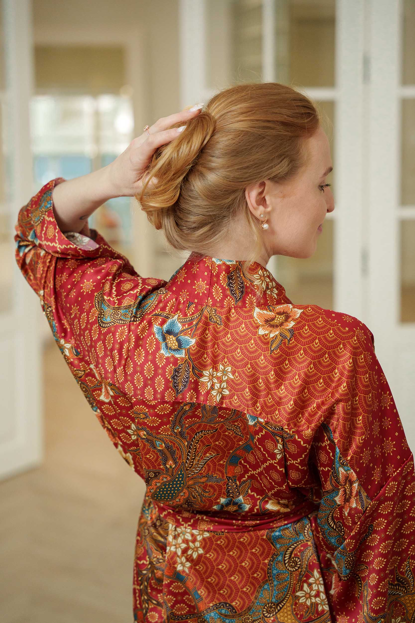 Back view of Toré Senja kimono robe – soft red satin fabric with intricate gold and teal batik details.