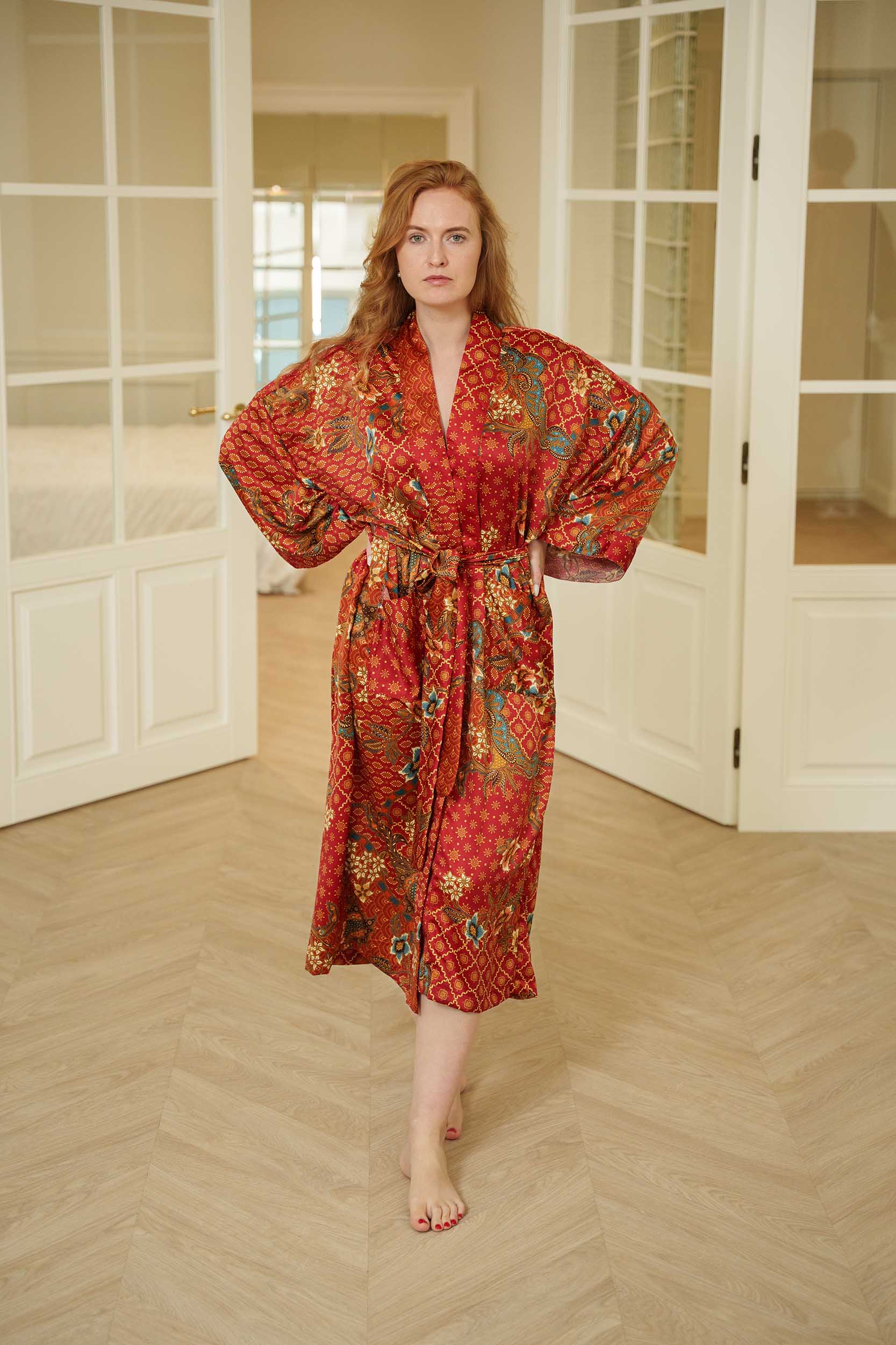 Woman wearing Toré Senja kimono robe – red satin long dressing gown with golden floral batik design.