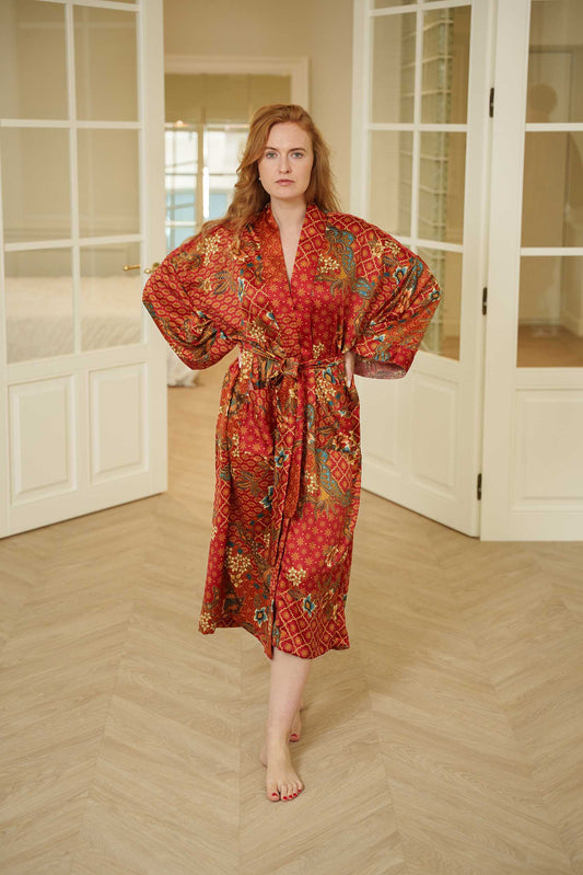 Woman wearing Toré Senja kimono robe – red satin long dressing gown with golden floral batik design.