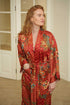 Woman wearing Toré Senja kimono robe – red luxury dressing gown with golden floral batik design.