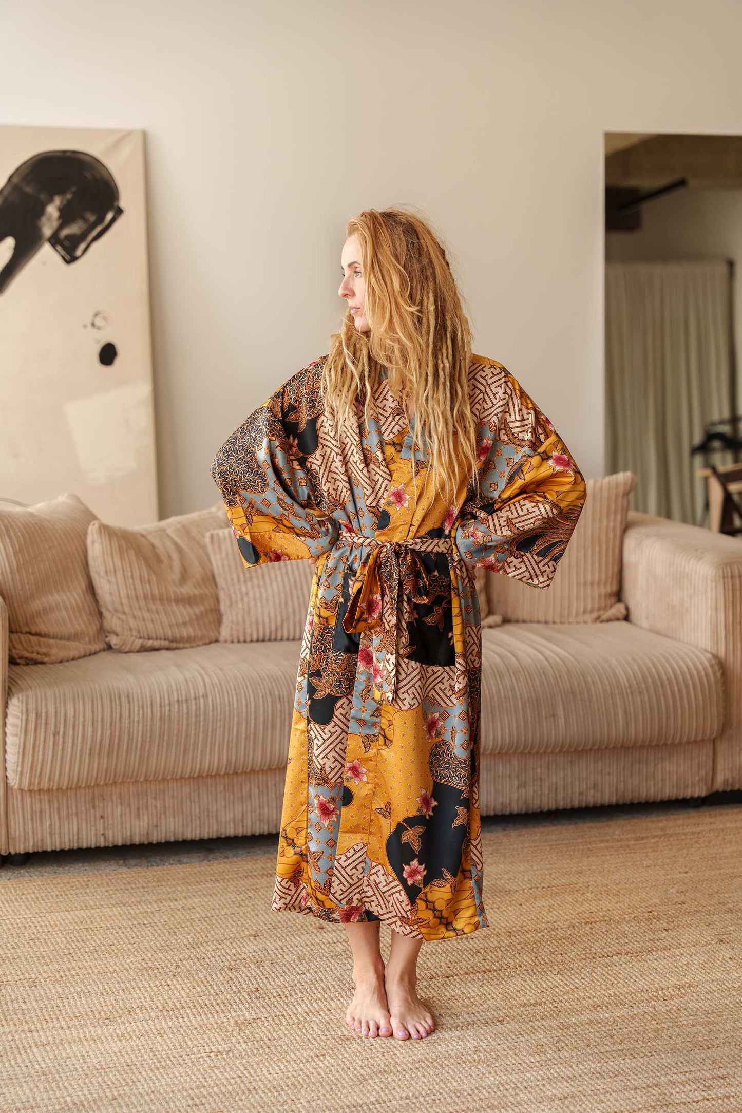 Woman wearing Toré Sorga kimono robe – long yellow and blue satin dressing gown with Indonesian batik design.