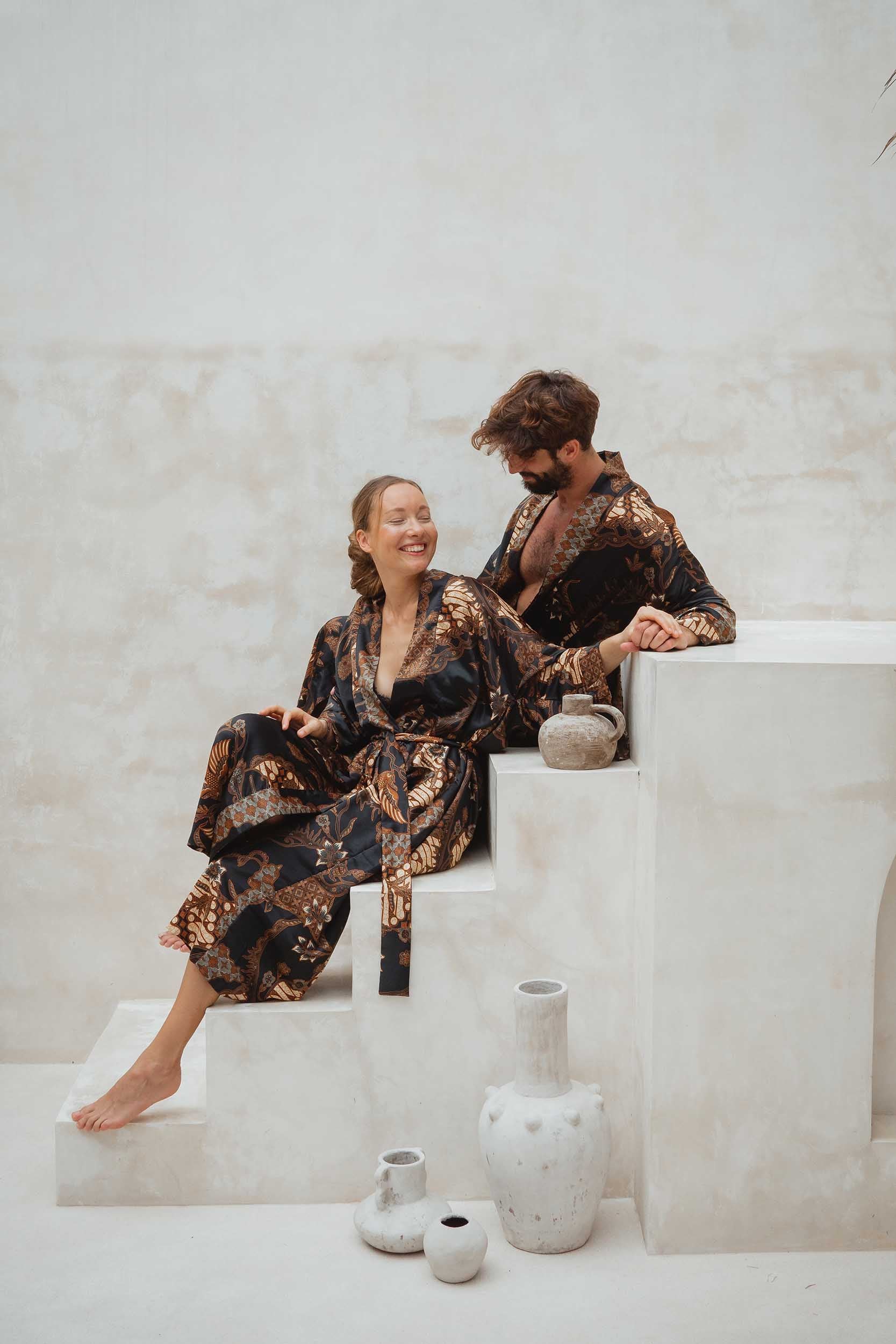 Couple wearing Toré Svarna kimono robes – black and gold satin robes with matching batik pattern.