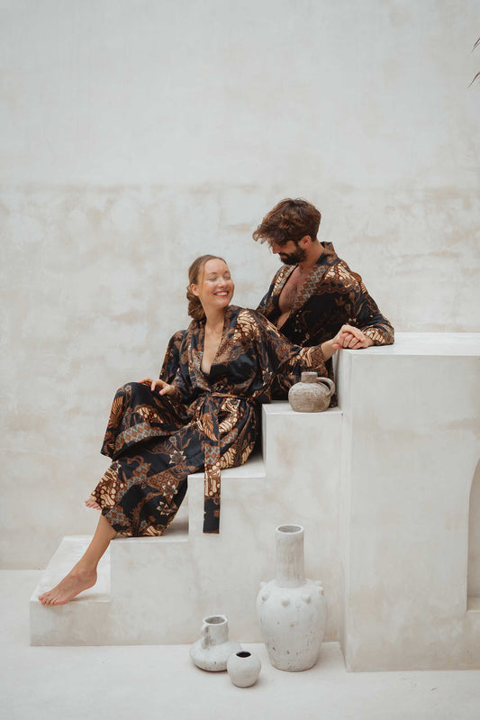 Couple wearing Toré Svarna kimono robes – black and gold satin robes with matching batik pattern.