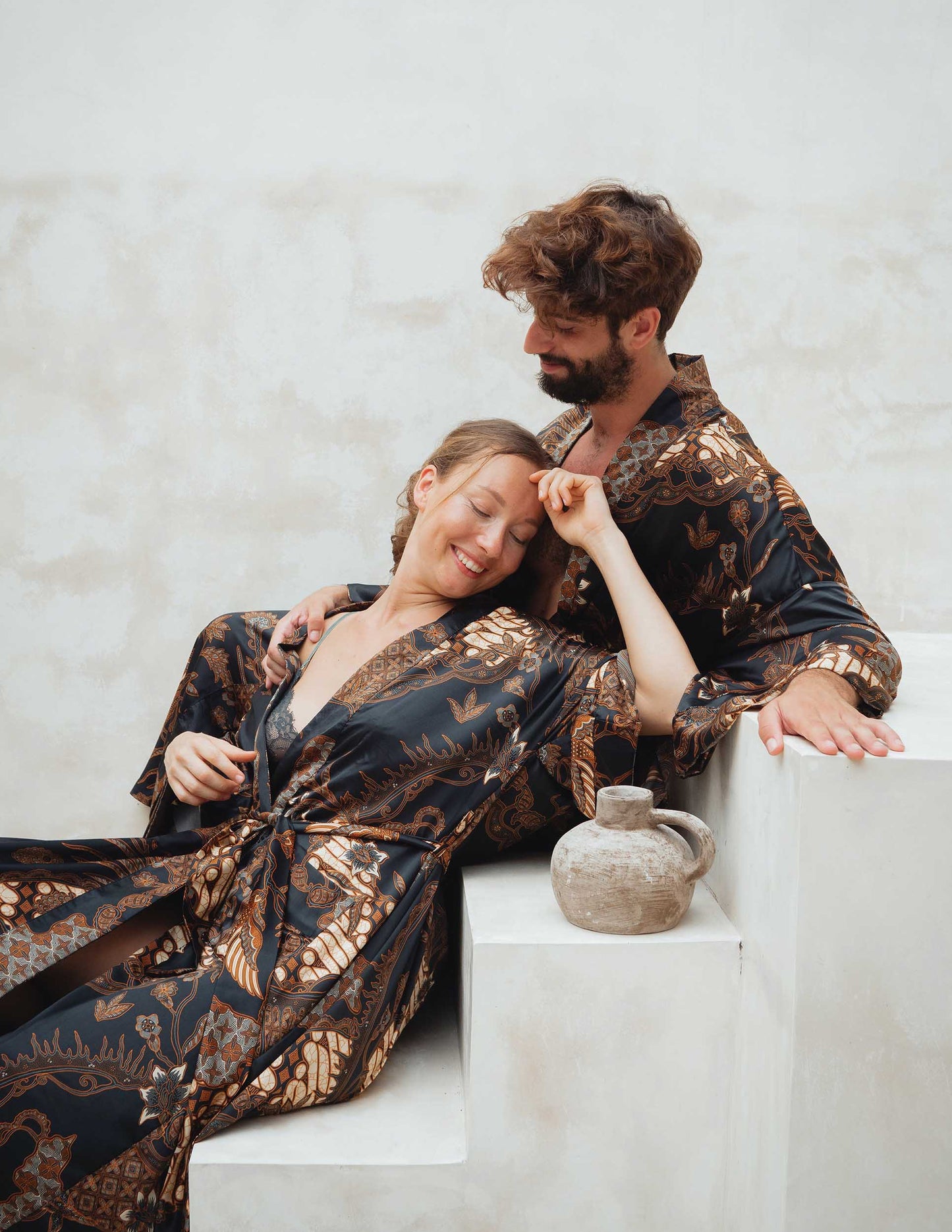 Man and woman in Toré Svarna robes – elegant couple kimono set in luxury satin fabric.