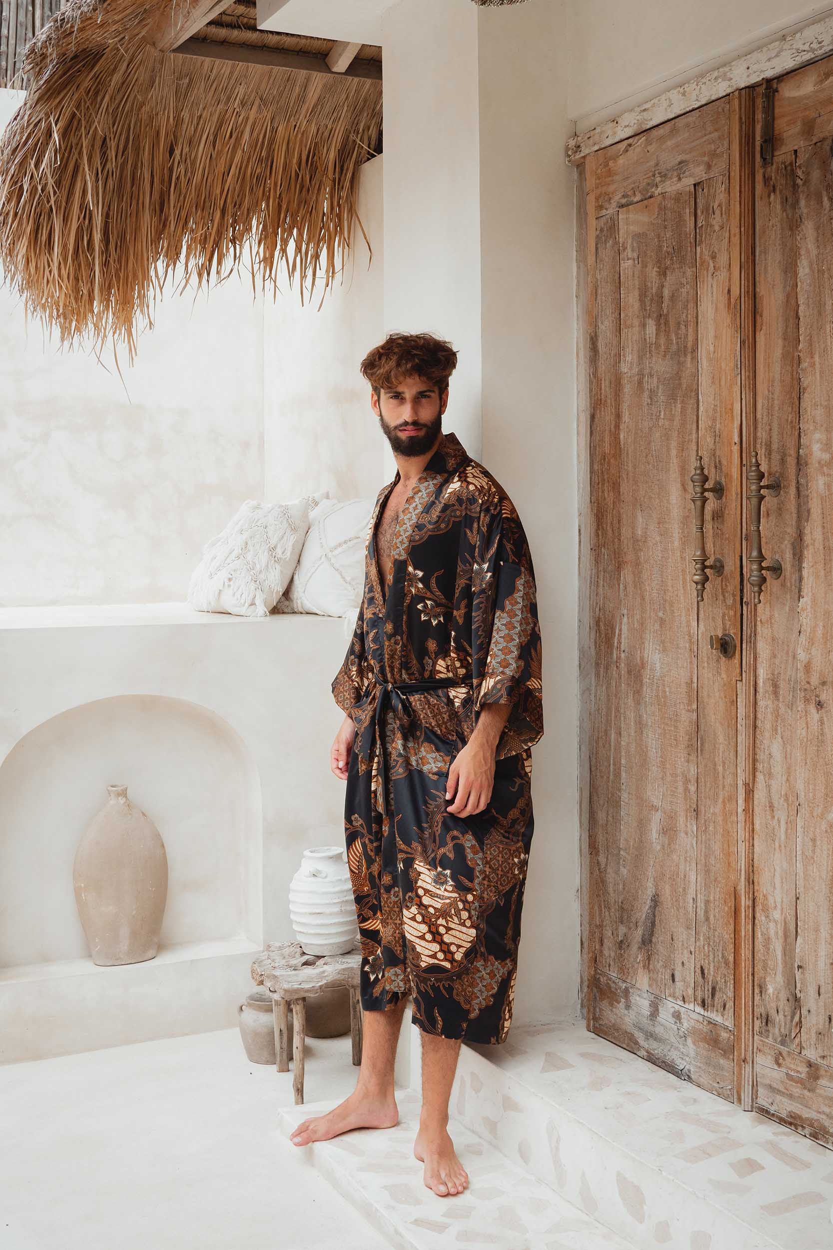 Man wearing Toré Svarna kimono robe – long black and gold satin dressing gown with batik pattern.
