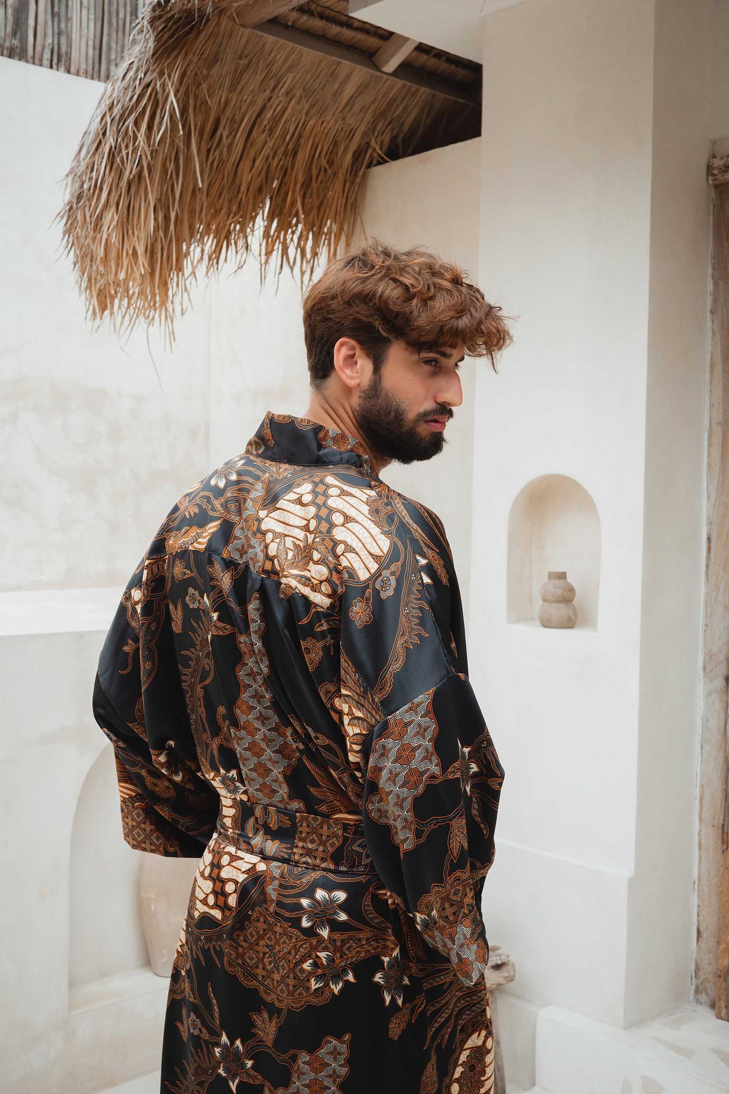 Close-up of Toré Svarna robe fabric – black satin with intricate bronze and gold batik print.