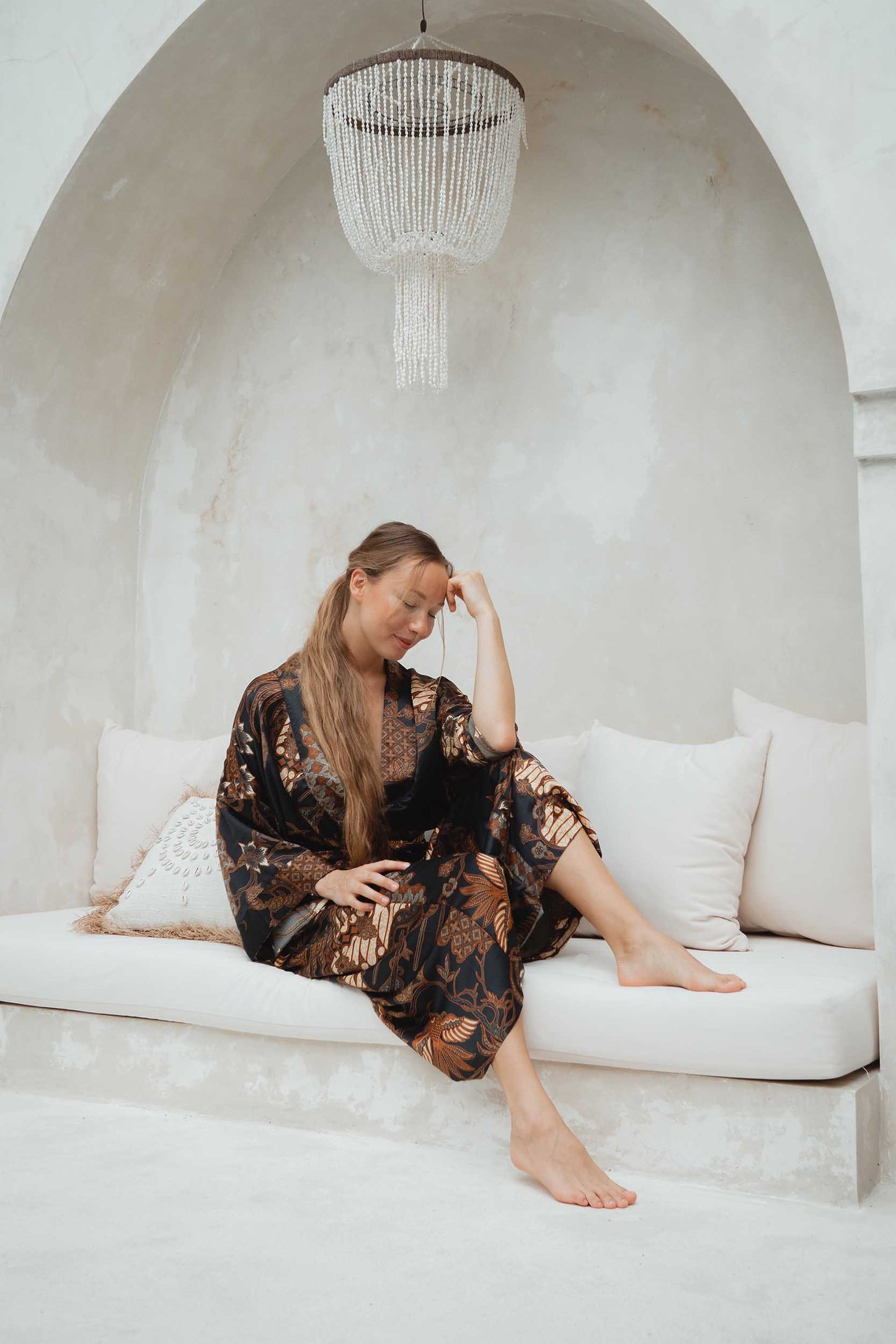 Woman wearing Toré Svarna kimono robe – long black and gold satin dressing gown with batik motifs.