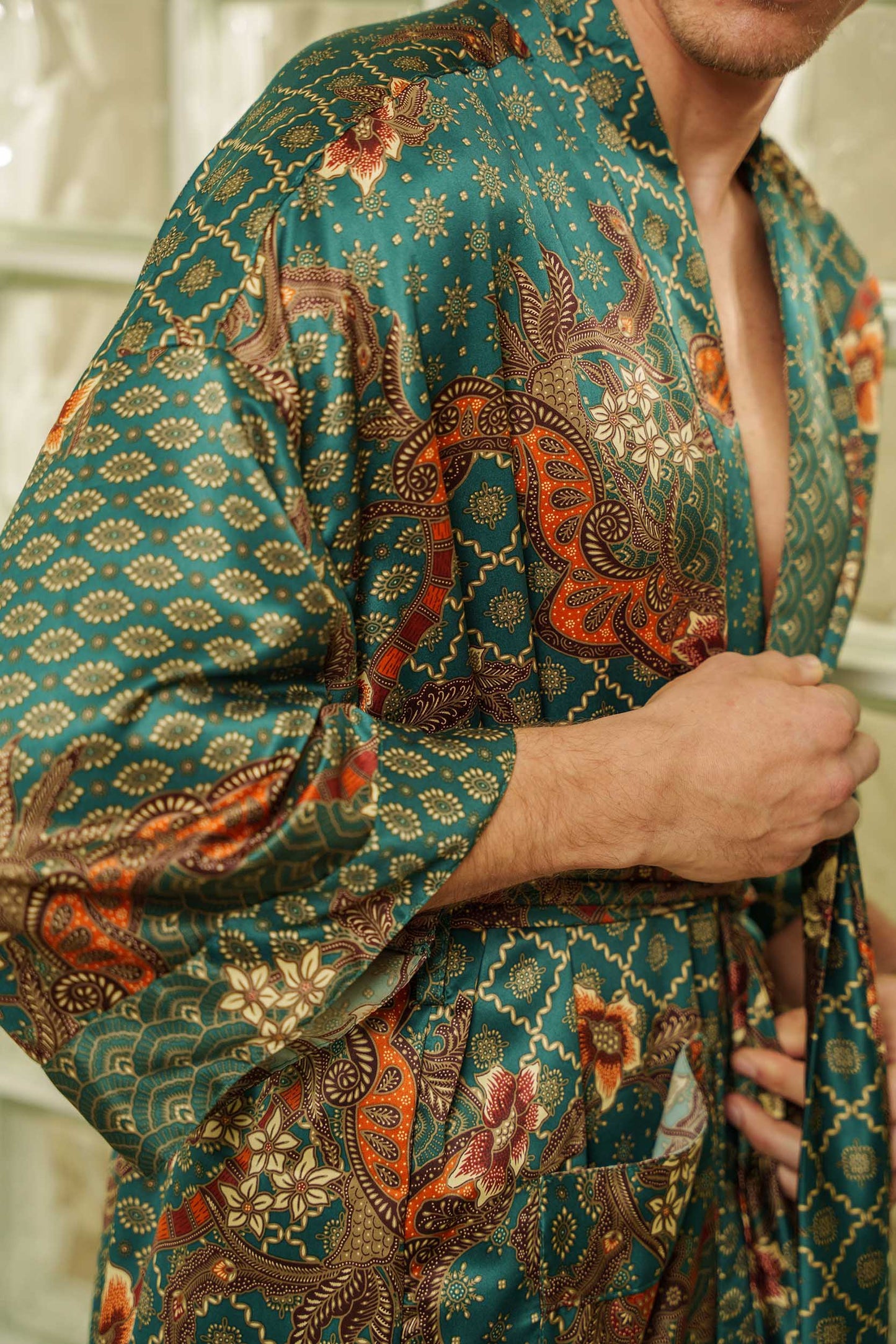Close-up of Toré Zamrud robe fabric – emerald satin with floral and geometric batik patterns.
