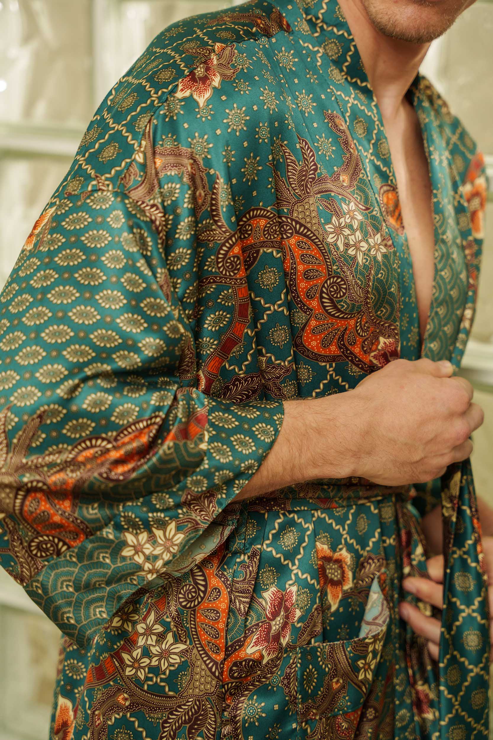 Close-up of Toré Zamrud robe fabric – emerald satin with floral and geometric batik patterns.