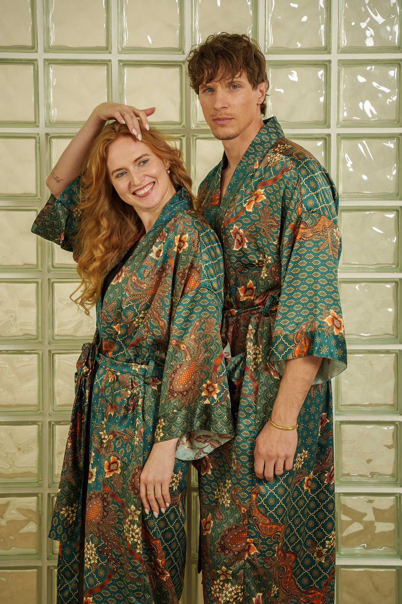 Couple wearing matching Toré Zamrud kimono robes – elegant emerald-teal satin dressing gowns with Indonesian batik motifs.