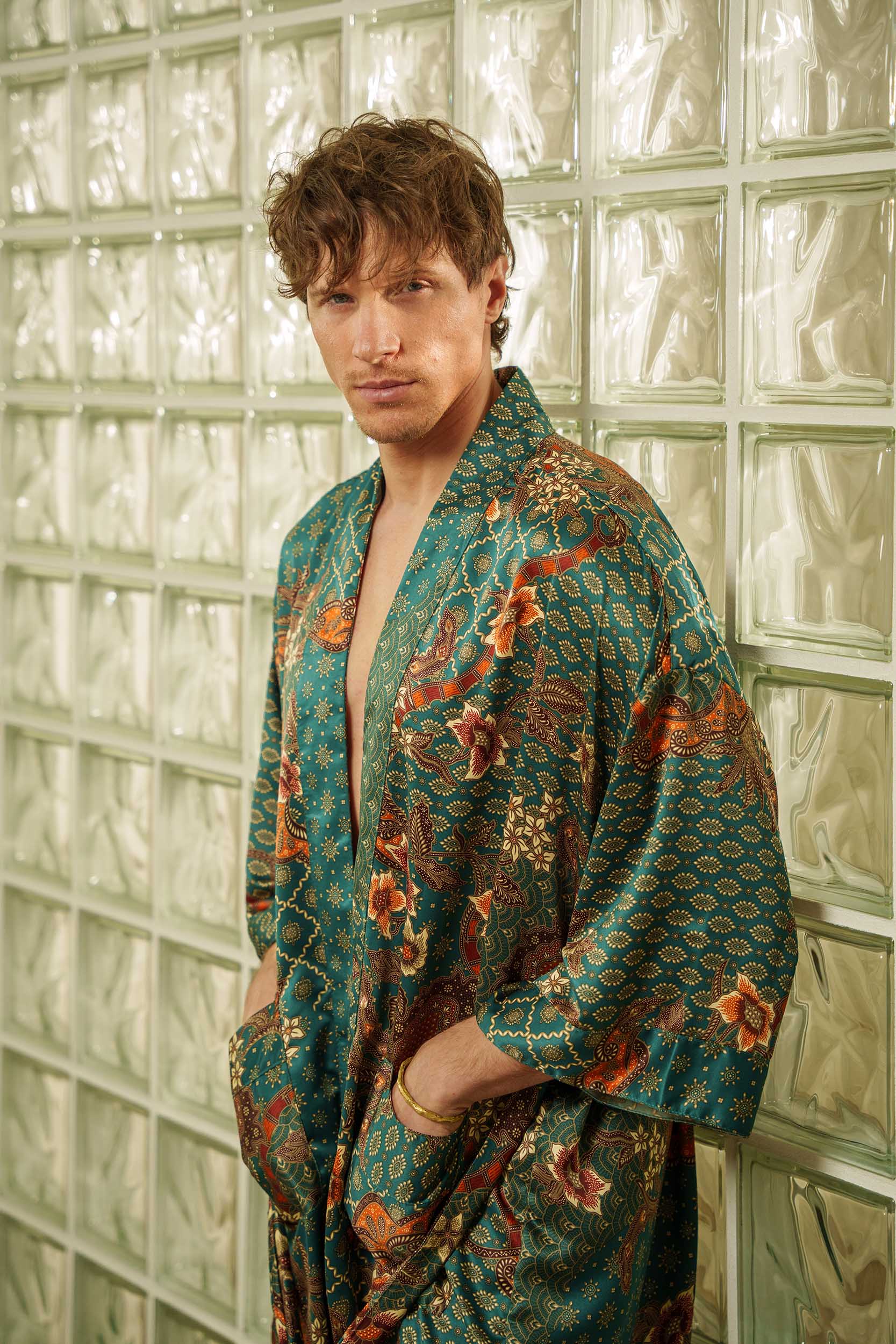 Man wearing Toré Zamrud kimono robe – luxury emerald teal satin dressing gown with Indonesian batik motifs.