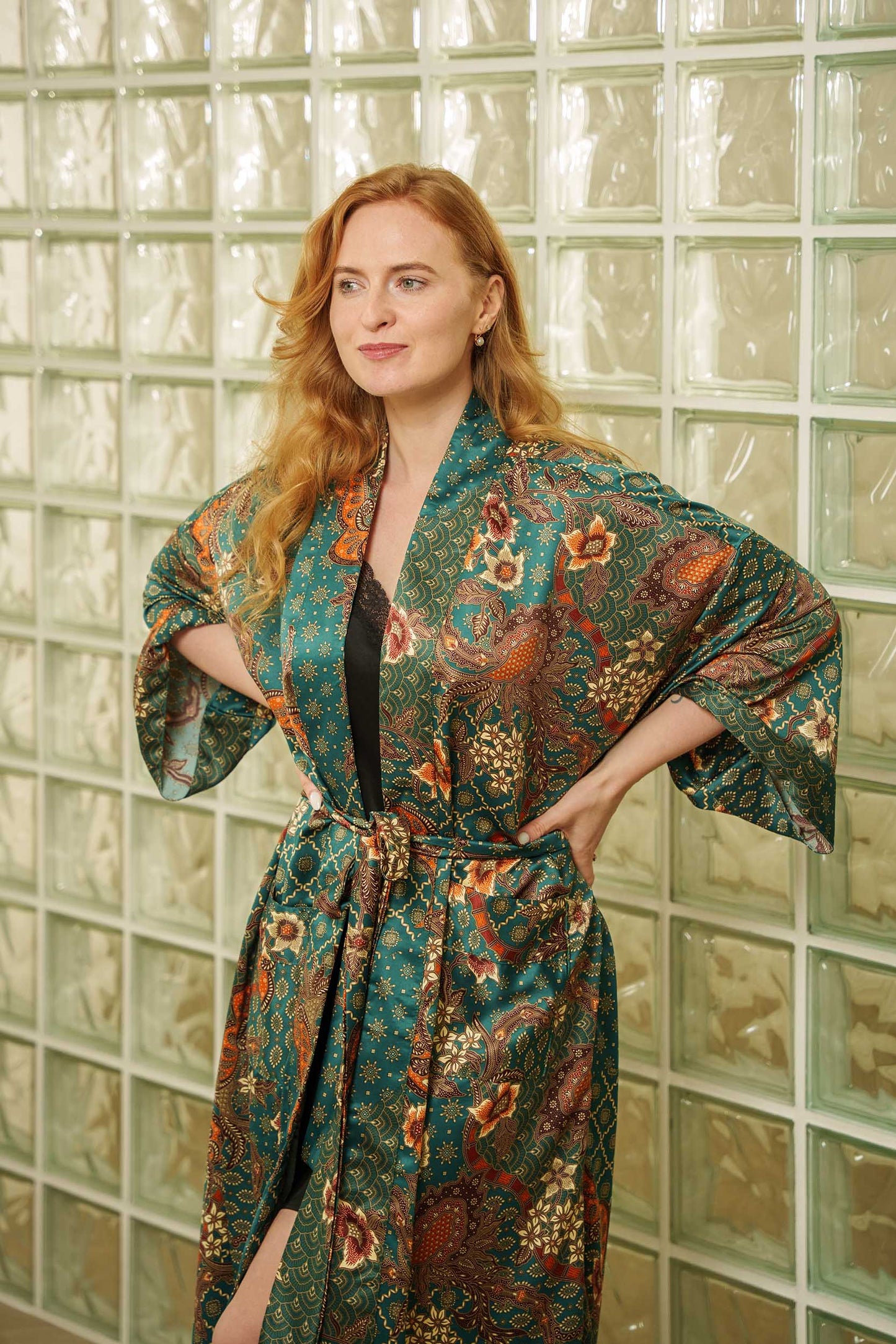 Woman wearing Toré Zamrud kimono robe – emerald teal satin dressing gown with gold batik motifs.